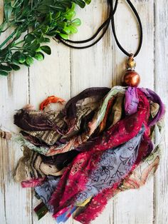 an assortment of scarves laid out on top of a white wooden table with greenery