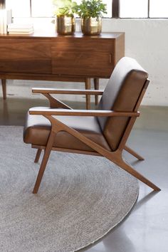 a chair sitting on top of a rug in front of a dresser and table with plants