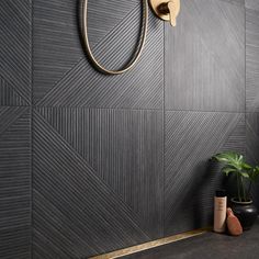 a bathroom with black tile and gold trim on the shower faucet next to a potted plant