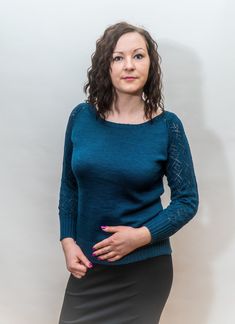 a woman standing in front of a white wall wearing a blue sweater and black skirt