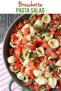 a pan filled with pasta and tomatoes on top of a wooden table next to a napkin