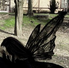 a woman with long black hair is standing in front of a tree and looking down at the ground