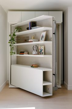 a white book shelf with books and plants on it in a room that has hardwood floors