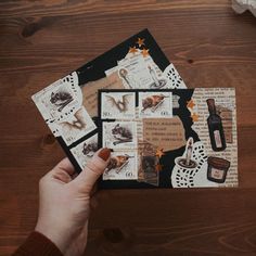 a person is holding up some stamps on top of a table with other items in front of them