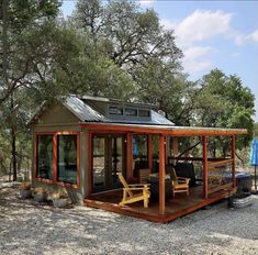 a small house with a porch and covered patio in the middle of a wooded area