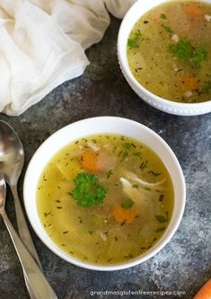 two bowls of soup with carrots and parsley on the side next to a spoon