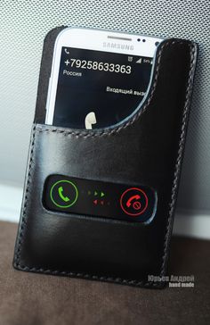 a cell phone in a leather case with buttons on the front and back side, sitting next to a wall