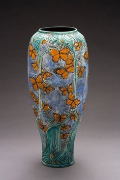 a blue vase with orange butterflies on the top and bottom, sitting on a gray surface