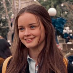 a girl with long brown hair and blue eyes smiles at the camera in front of christmas decorations