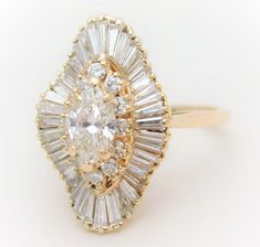 "From an elegant New Orleans estate. This dazzling ring is made of solid 14k yellow gold. The style of this unique cluster-style ring is called ballerina due to all of its tapered baguettes flowing like a ballerina's skirt. The style represents a style in jewelry making long forgotten. Bright and sparkling, it is masterfully jeweled with a total of 53 amazing diamonds. The GIA certified center stone (#6157498699) is a Marquise-Brilliant shaped diamond with a J color/VVS2 clarity. Surrounding the Ballerina Engagement Ring, Platinum Engagement Rings Vintage, Ballerina Ring, Vintage Cluster Ring, Marquise Diamond Engagement Ring, Contemporary Engagement Rings, Modern Engagement Rings, Cluster Rings, Dream Engagement