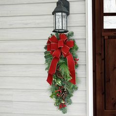 a christmas wreath hanging on the side of a house next to a lamppost with a red bow