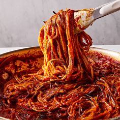 spaghetti being cooked in a skillet with a ladle full of sauce and noodles