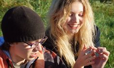 two young people sitting on the grass looking at their cell phones, one is smiling