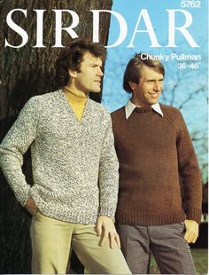 two men standing next to each other in front of a tree and wearing sweaters