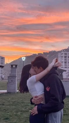 a young man and woman kissing in front of a sunset over the cityscape