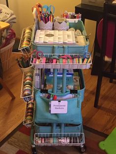 a cart filled with lots of craft supplies on top of a wooden floor next to a table