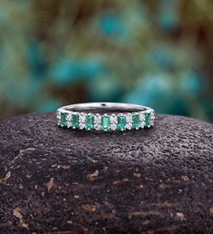 an emerald and diamond wedding band on top of a rock with trees in the background