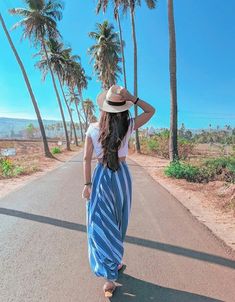 a woman walking down the middle of a road with palm trees in the back ground