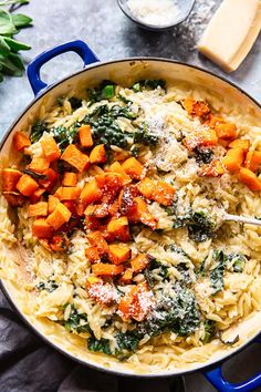 a blue pot filled with pasta and vegetables on top of a table next to cheese