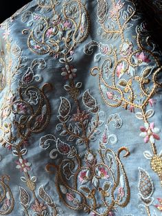 the back of a blue dress with gold and pink flowers on it