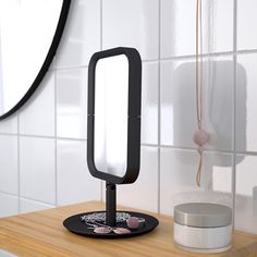 a mirror sitting on top of a wooden table next to a white tiled bathroom wall