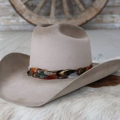 The Vistoso Western Feather Hat Band, with a 3 cm width and approximately 58 cm in length (not including leather ties), offers both versatility and style. This one-size-fits-most accessory is adjustable with leather ties, allowing for a comfortable and secure fit. The feather detailing adds a vibrant touch, making it a standout piece that effortlessly enhances any hat with a hint of western charm. Adjustable Leather Top Hat With Curved Brim, Adjustable Leather Fedora, Adjustable Western Hat Bands For Fall, Adjustable Hat Bands For Country Events In Fall, Adjustable Country Hat Bands For Fall, Rustic Adjustable Felt Hat With Short Brim, Classic Hat With Adjustable Leather Sweatband, Adjustable Hat Bands For Fall Outdoor Events, Classic Adjustable Hat With Leather Sweatband