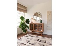 a living room with a rug, mirror and potted plant on the sideboard