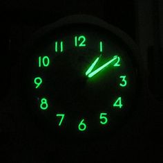 an illuminated clock in the dark with green numbers on it's face and hands