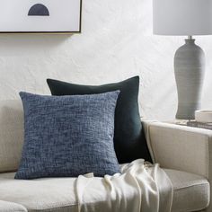 a couch with two pillows on it next to a lamp and pictures hanging on the wall