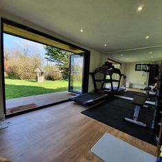 a home gym with treadmills, exercise mats and large windows looking out onto the yard