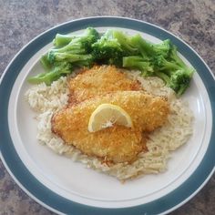 a plate with chicken, rice and broccoli on it next to a lemon wedge