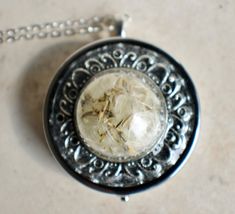 a silver necklace with a glass ball in the center on a marble surface and a chain attached to it