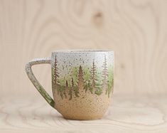 a coffee cup with trees painted on the outside and inside, sitting on a wooden surface