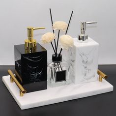 marble and gold bathroom accessories on a black counter top with white flowers in vases