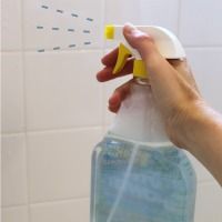 a hand is holding a spray bottle in front of a tiled wall with blue and white tiles