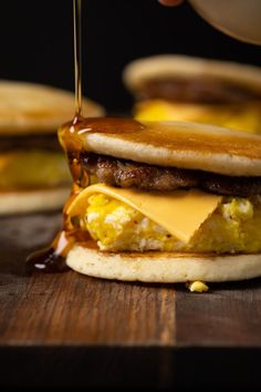 someone is drizzling cheese on top of a sausage and egg breakfast sandwich