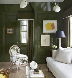 a living room with green walls and white furniture in the corner, along with paintings on the wall