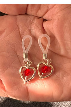 a pair of red heart shaped earrings on a person's hand