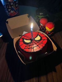 a birthday cake with a spiderman face on it and a candle in the middle