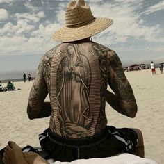 a man sitting on the beach with his back to the camera, wearing a straw hat