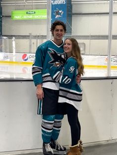 a man and woman standing next to each other in front of an ice hockey rink