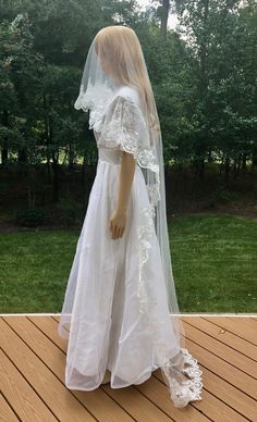 a mannequin wearing a wedding dress and veil on a deck in front of trees