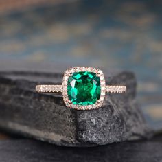 a ring with a green stone surrounded by white diamonds on top of a black rock