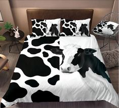 a black and white cow is laying down on a bed with two pillow cases in front of it