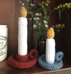 two crocheted candles sitting on top of a wooden shelf