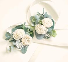 two white roses and greenery on top of each other next to a ribbon bow