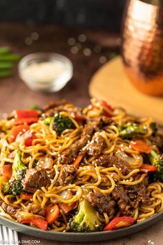 a plate full of noodles with beef and broccoli in it on a table