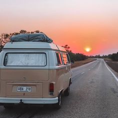 an old vw bus is parked on the side of the road as the sun sets