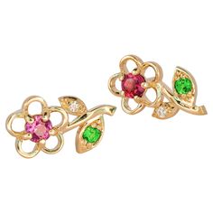 14 karat gold earrings studs with genuine garnets, tsavorites and diamonds. January birthstone. Metal: 14 karat gold. Weight: 1.95 g. Size: 13 x 6 mm. Central stones: Genuine garnets: weight - 0.08 ct x 2 = 0.16 ct total, red and purple color. Round cut, clarity good - small inclusions. Surrounding stones: Genuine tsavorites: 2 pieces, weight - 0.04 ct x 2 = 0.08 ct total, green color. Round cut, clarity good - small inclusions. Diamonds: G/VS, round brilliant cut, 2 x 0.01 ct = 0.02 ct total in both earrings. Earrings goes with a plastics clasps. January Birthstone Jewelry, Garnet And Gold, Bracelet Love, Red And Purple, Earrings Metal, Earrings Studs, Design Earrings, Flower Earrings Studs, Modern Earrings