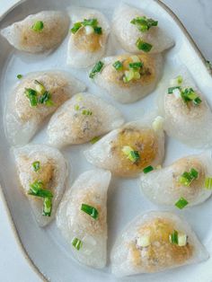 some dumplings are on a white plate with green onions and scallions in them